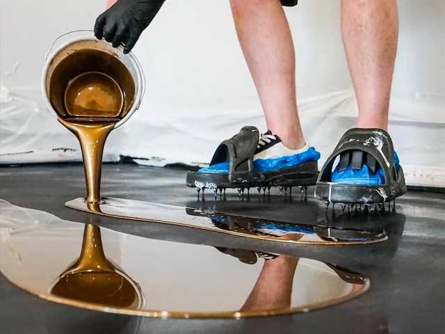 una persona con indosso scarpe speciali versa della resina da un contenitore per creare un pavimento in resina